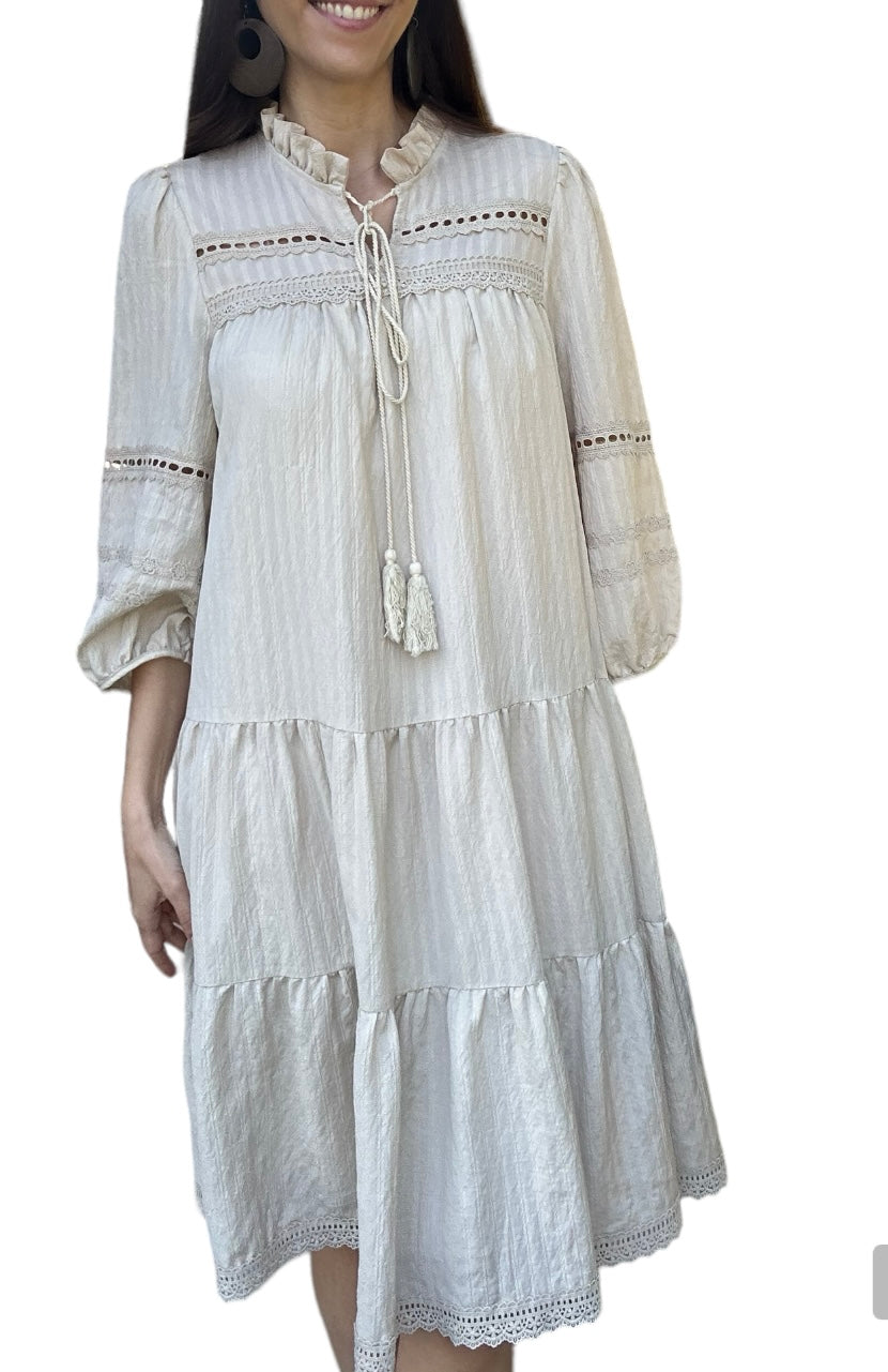 Robe d'été légère Daniella, élégante beige doublée avec des détails en dentelle et des broderies délicates. Cette robe à manches trois-quarts présente une encolure à cordon avec des pompons, ajoutant une touche bohème et décontractée.

La coupe ample et fluide est parfaite pour les journées chaudes, offrant confort et style. La robe est ornée de plusieurs volants, apportant du volume et du mouvement à chaque pas.