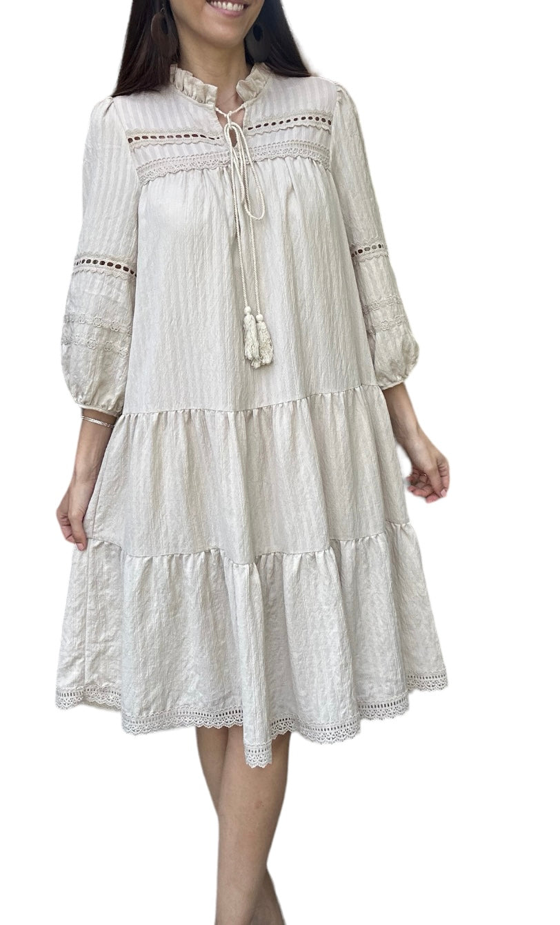 Robe d'été légère Daniella, élégante beige doublée avec des détails en dentelle et des broderies délicates. Cette robe à manches trois-quarts présente une encolure à cordon avec des pompons, ajoutant une touche bohème et décontractée.

La coupe ample et fluide est parfaite pour les journées chaudes, offrant confort et style. La robe est ornée de plusieurs volants, apportant du volume et du mouvement à chaque pas.